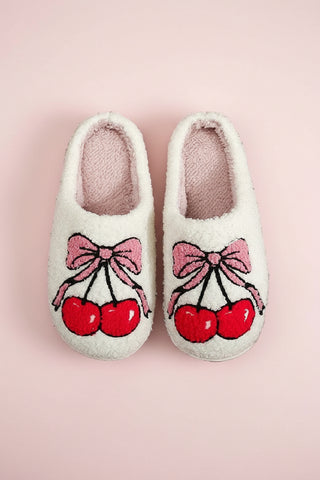 Pair of white slippers with cherry and bow design on a white background
