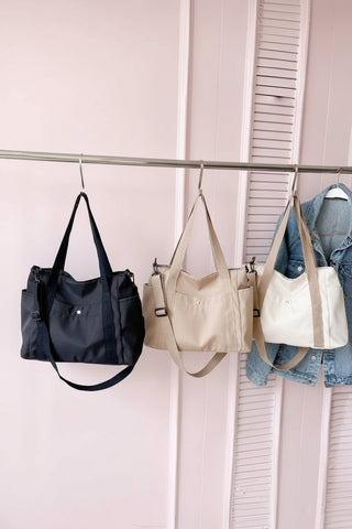 Four handbags hanging on a rack against a white wall.